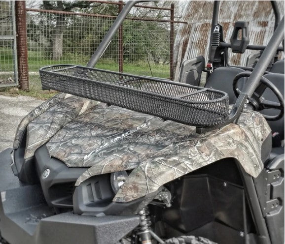 A Yamaha ATV with a camouflage pattern is parked by a fence and metal building. It features a large, rectangular black Yamaha Viking Roll Bar Basket (Bolts On Factory Frame) mounted on the front for carrying cargo.