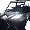 A black off-road utility vehicle with angular, rugged design, roll cage, two visible seats labeled “RZR,” and “1000” marking on the side. The windshield is partially open, and the sunlight reflects brightly off the vehicle’s front panel.