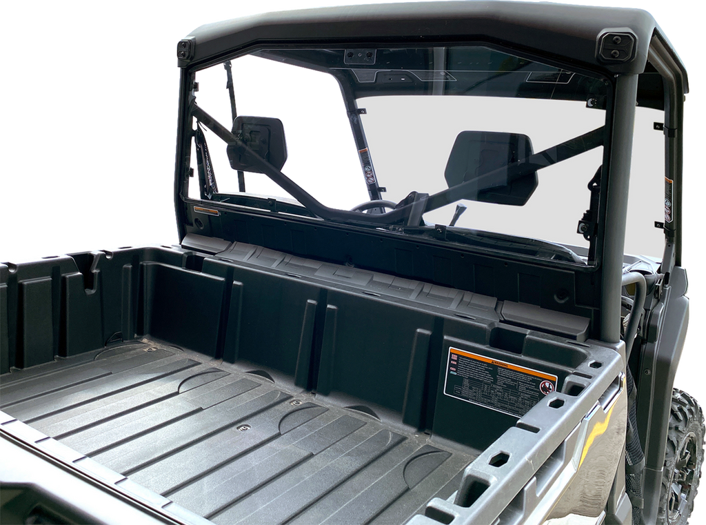 Close-up view of the empty rear cargo bed of a black utility task vehicle (UTV). The image shows the rear window, roll cage, and interior seats through the glass, with warning labels visible on the side of the cargo bed.