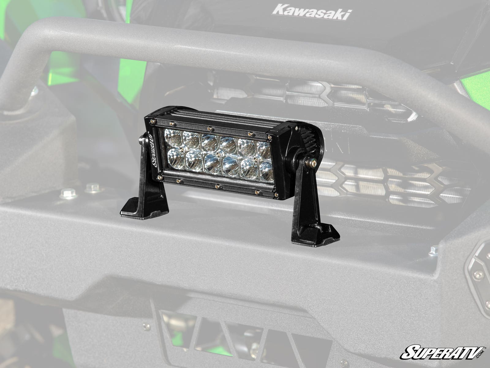 A 6 LED Combination Spot / Flood Light Bar is mounted on the sturdy, matte black front bumper of a green Kawasaki off-road vehicle. The SuperATV logo appears in the lower right corner.