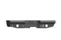The 1999-2016 Ford F-250 Vaquero Rear Non-Winch Bumper in textured black features an angular metal design with bolt holes and square cutouts, a circular logo on the right, and rounded ends for a rugged, heavy-duty look.