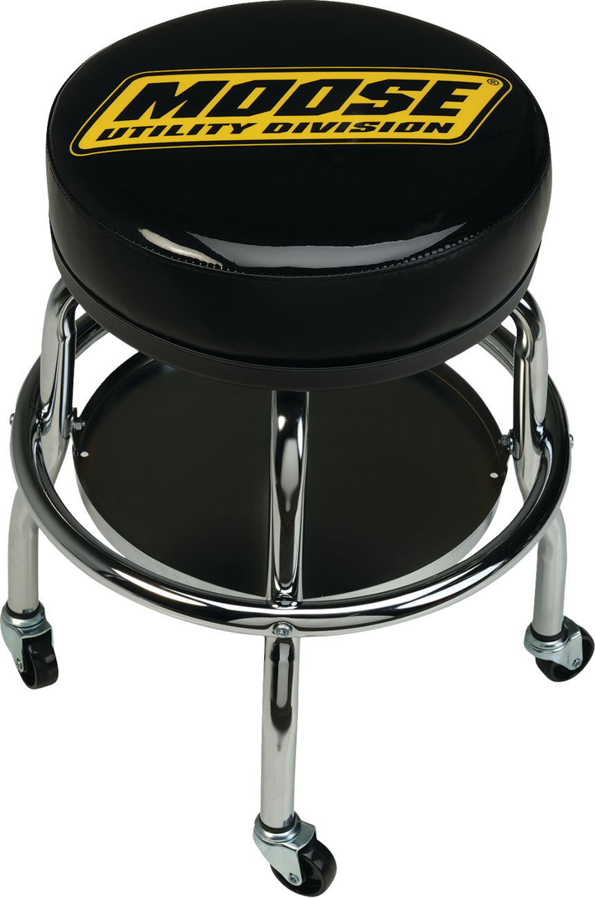 A black, round stool with a chrome frame and caster wheels. The cushioned seat features the yellow MOOSE UTILITY DIVISION logo in bold, block letters. A circular footrest and lower black support shelf are visible between the stool’s legs.