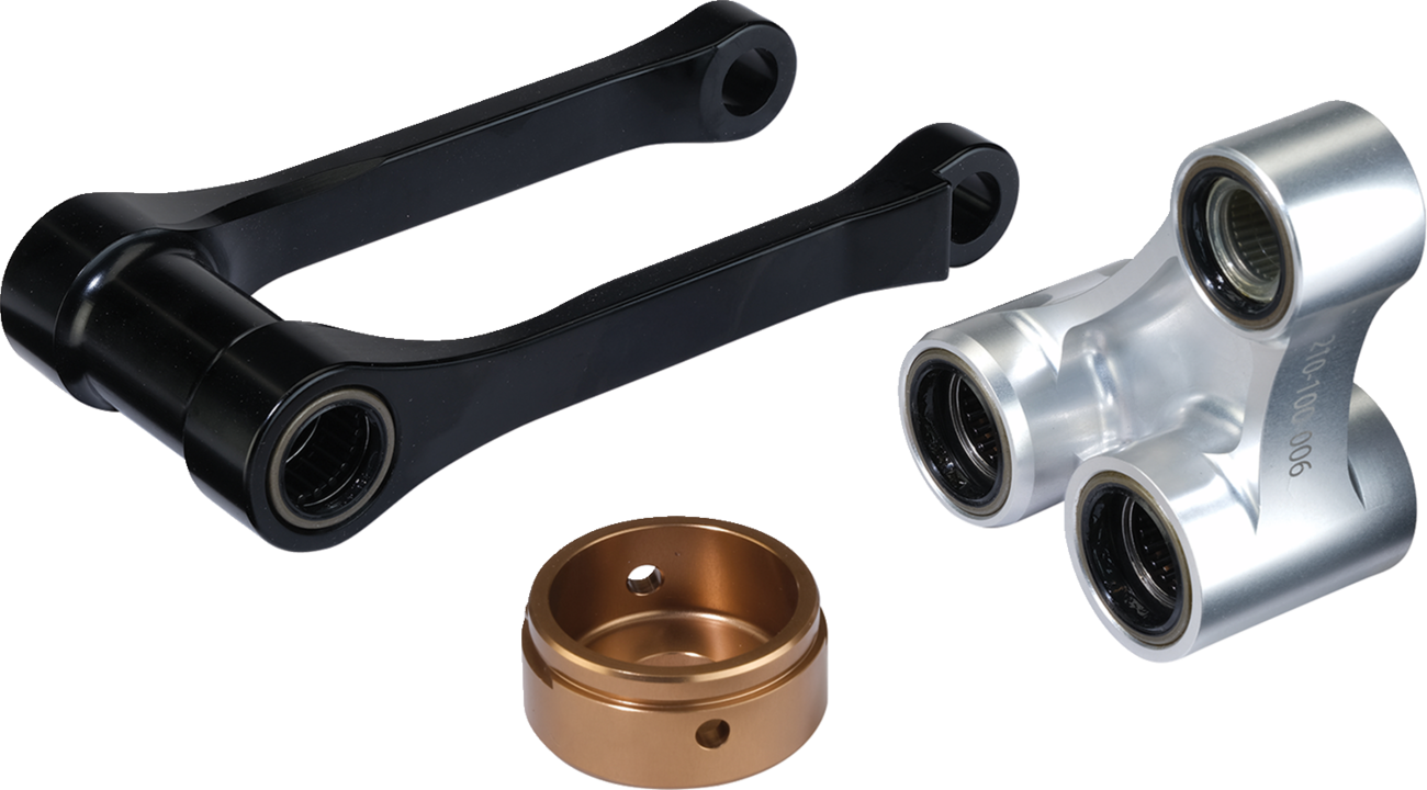 Three mechanical parts: a black U-shaped linkage with bearing holes at each end, a silver triple-connector component with three circular openings containing bearings, and a round bronze-colored cap with a central hole and side groove. All parts are metall