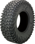 A large, rugged off-road tire stands upright against a white background. The tire has deep, aggressive treads and chunky sidewalls designed for enhanced grip on rough terrain. Faint embossed branding and tire specifications are visible on the side.