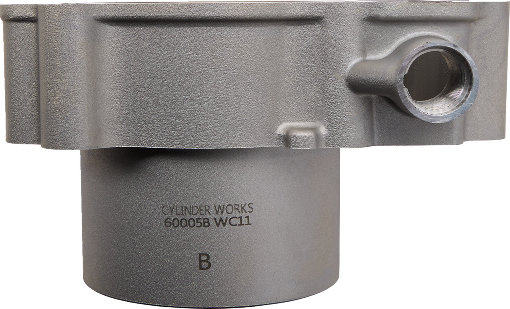 Close-up of a metallic cylindrical engine part with a side opening and engraved text reading CYLINDER WORKS 60005B WC11 B on the smooth lower section. The upper section is thicker and features a rounded extension. The background is plain white.
