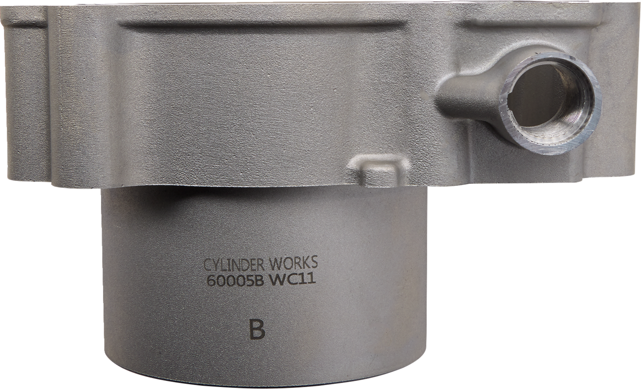 Close-up of a metallic cylindrical engine part with a side opening and engraved text reading CYLINDER WORKS 60005B WC11 B on the smooth lower section. The upper section is thicker and features a rounded extension. The background is plain white.