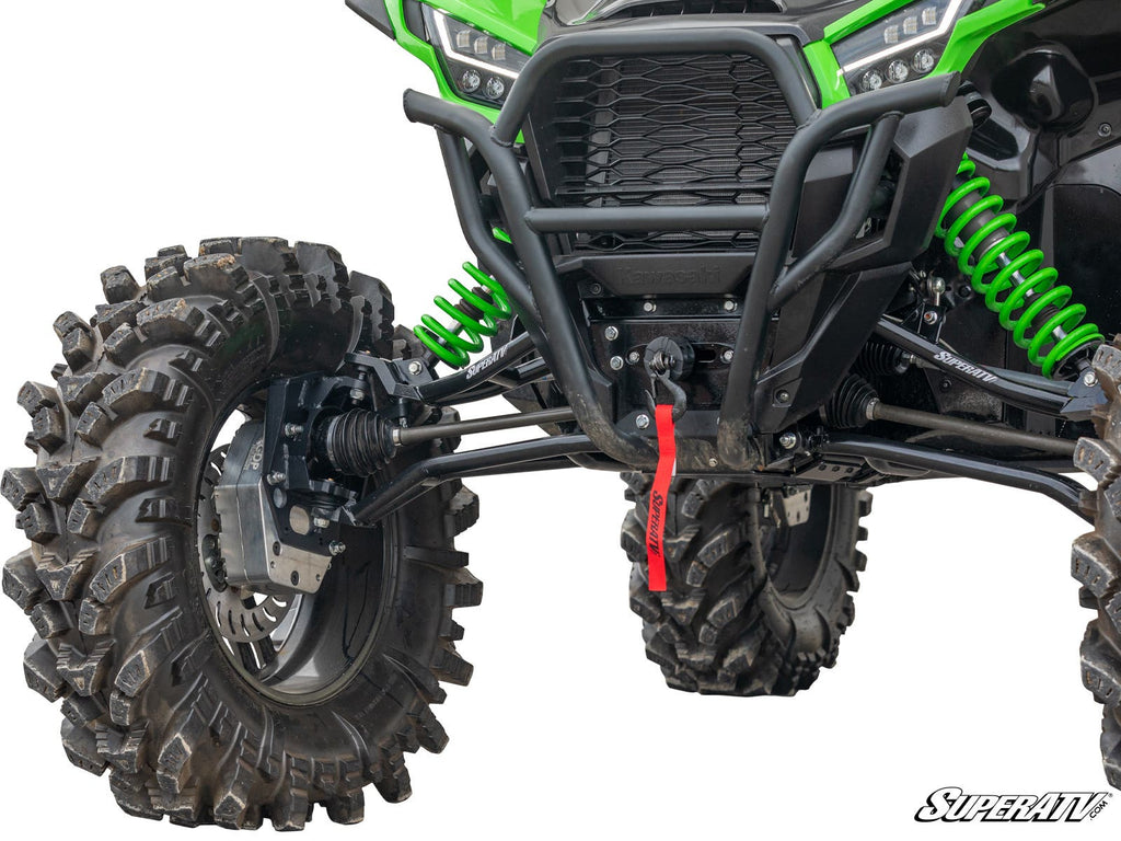 Close-up of a Kawasaki Teryx KRX 1000 with a 6 Portal Gear Lift, featuring large mud tires, green coilover shocks, a black bumper, and a red tow strap. The SuperATV logo appears in the bottom right corner.