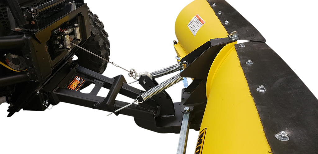 Close-up of a yellow snow plow blade attached to the front of a vehicle. The plow is secured with metal springs and bolts, and features a black mounting bracket. The setup is designed for clearing snow, with visible mechanical connection details.