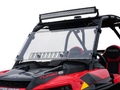 A close-up of a red Polaris RZR Turbo S (2018+) with a black frame, overhead LED light bar, RZR-branded black seats, angular styling, and a Rzr Turbo-S Scratch Resistant Venting Windshield.