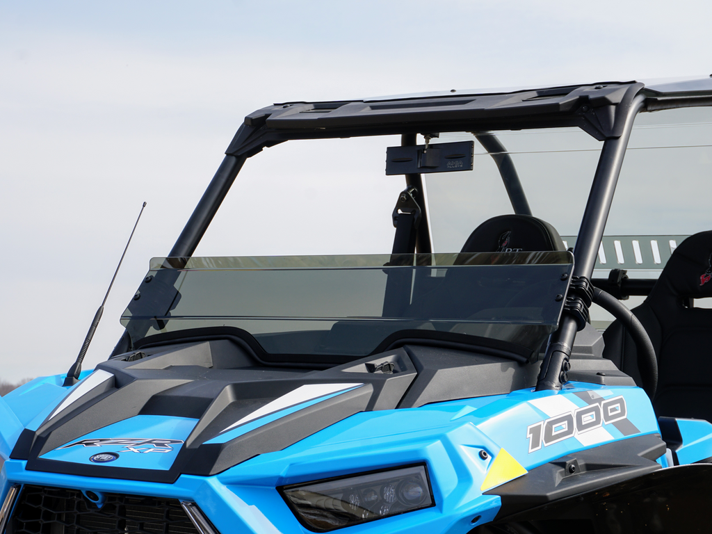A close-up of the Polaris Rzr Turbo-S and 2019 XP1000 with a short tinted windshield highlights its angular headlights, black frame, and dashboard. The clear sky with light clouds forms the background.