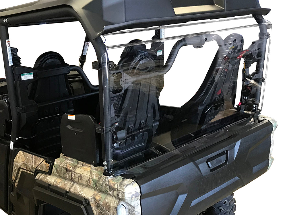 A close-up of the Yamaha Wolverine X-4 Rear Windshield-Gp 2015+ shows two black seats, a clear polycarbonate rear windshield, camouflage body panels, and a roll cage—all highlighting its rugged off-road design against a white background.
