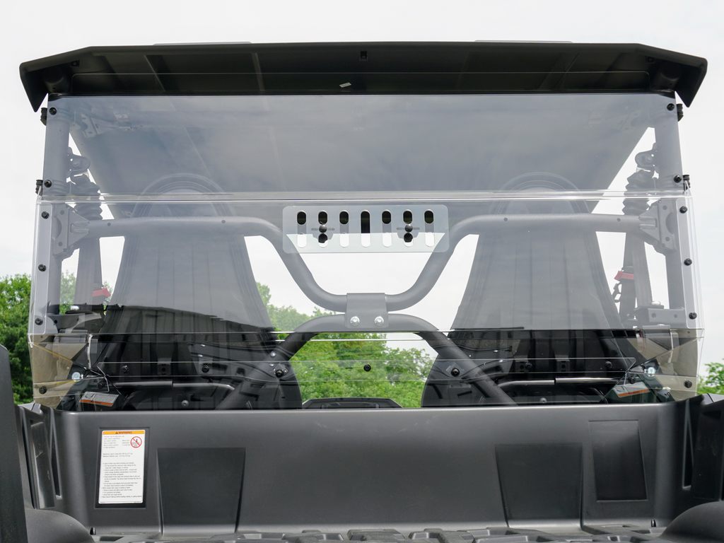 A Yamaha Wolverine X-2 Rear Windshield-Vented-Gp is installed on a black 2019-20 Wolverine X-2 utility vehicle, revealing two black bucket seats inside with green trees and a cloudy sky visible through the clear rear windshield.