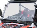 A Polaris Rzr 570/800/900 Scratch Resistant Full Venting Windshield with flip clamp and black mounting brackets is installed on an off-road vehicle with orange and black seats, showing the roll cage and harness through the windshield.