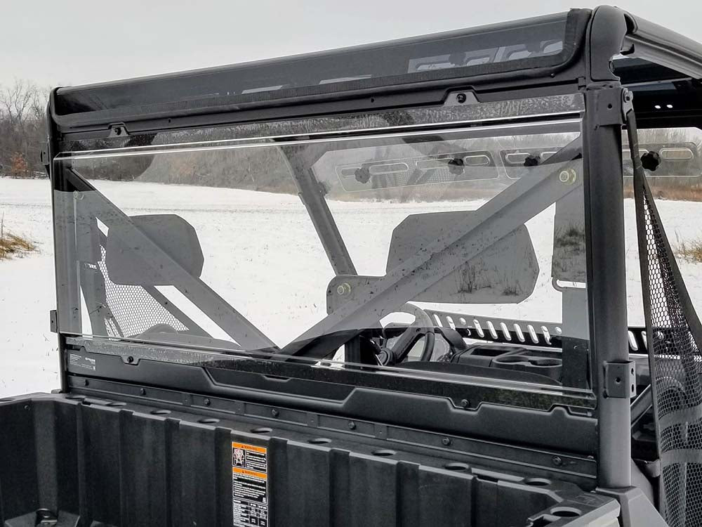 A Polaris Ranger Full Size (Profile Tubing) Rear Window–Hard Coated Scratch Resistant—all 2013+ models—is installed on a UTV with two headrests, parked on snowy ground among leafless trees under an overcast sky, framed by a black metal roll cage.
