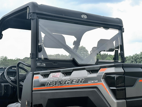 A close-up shows a 2019+ Polaris Ranger 1000/XP fitted with a Spike Powersports rear windshield, featuring the “SPIK” label. The bold “RANGER” logo is on the front, with trees and sky visible in the background.