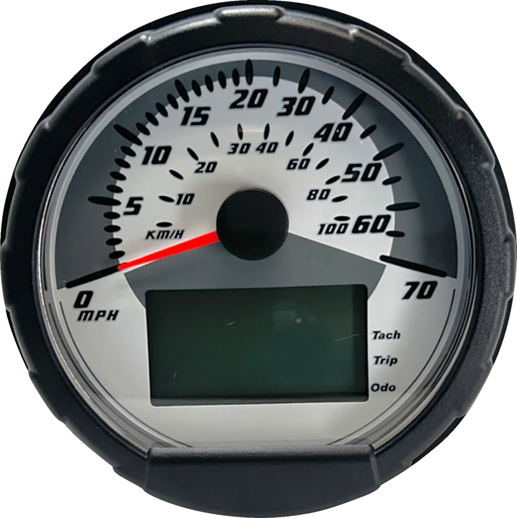 A close-up of a round speedometer with a black outer rim. The dial shows speeds from 0 to 70 in large black numbers, labeled MPH, with a smaller KM/H scale. A red needle points to 5 MPH. There is a digital display and indicators for tach, trip, and odo at