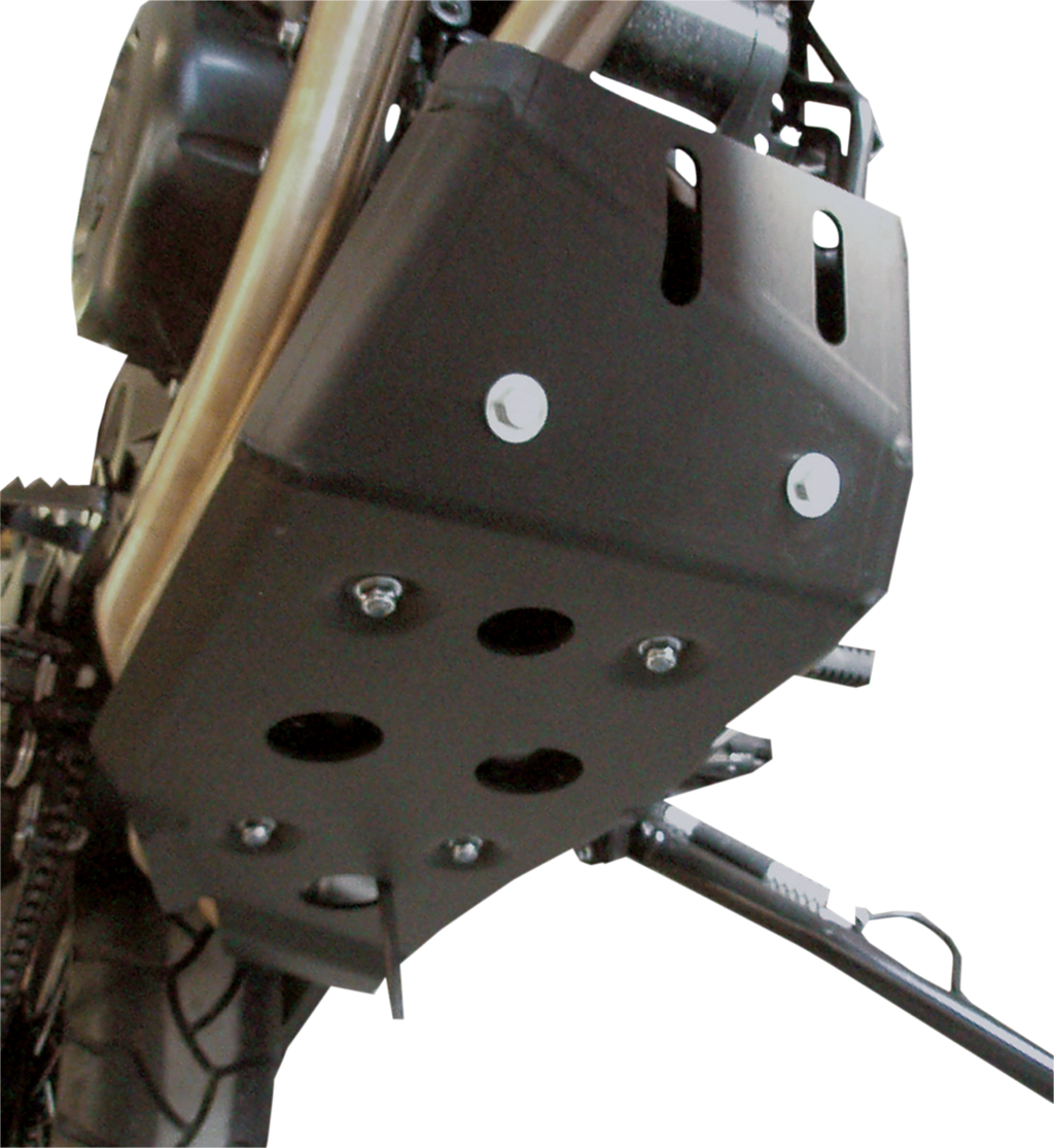 Close-up view of a black metal motorcycle skid plate mounted beneath the engine, featuring several bolts and round holes for ventilation or drainage. Part of the motorcycle’s tire and side stand are also visible. The background is plain and white.
