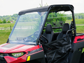 A Polaris Youth Ranger 150 with a hard coated scratch-resistant windshield, roof, and rear shield combo is parked on grass. The red off-road utility vehicle features a black frame, mesh side door, and two black bucket seats amidst trees and a cloudy sky.