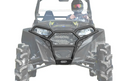 A helmeted driver in goggles operates a black off-road vehicle equipped with a Polaris RZR 800 Front Bumper and large, deep-tread tires, photographed head-on against a white background.