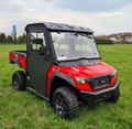 An Arctic Cat Prowler Pro 800/Textron Stampede with a Protector Cab Kit, black roof, rugged tires, side doors, sturdy front bumper, and clear windows is parked on green grass with buildings and trees in the background under a cloudy sky.