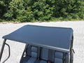 The Intimidator Single Cab Aluminum Top, in black, is installed over a four-seat utility vehicle with two-tone gray and black seats, shown parked on gravel against dense green trees and bushes.