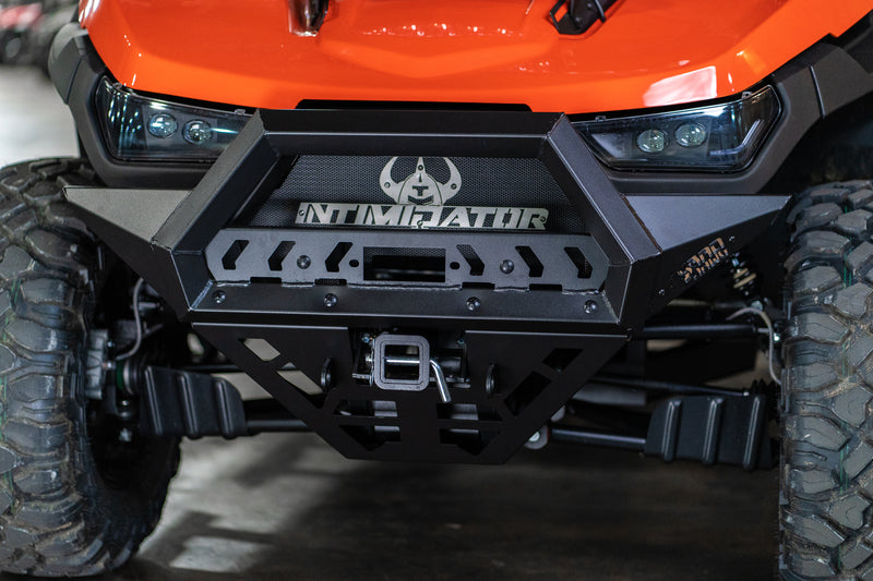 Close-up of the orange off-road vehicle’s Gc1K Front Bumper featuring INTIMIDATOR branding, a stylized bull logo, rugged tires, winch mount, black bumper, plus detailed suspension and headlight design.