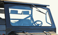 Close-up of a Gc1K Dot Glass Windshield installed on an off-road vehicle cab, featuring a clear windshield with single wiper, steering wheel, and two front seat headrests. The well-lit image shows a white background through the glass.