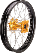 Close-up of a motorcycle wheel featuring a black rim, silver metal spokes, and a gold-colored hub. The rim displays white branding text, and the gold hub stands out with detailed machining and visible bolt holes. The background is plain white.