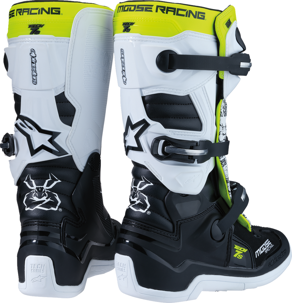 Two black, white, and neon yellow motocross boots with MOOSE RACING branding at the top, angular designs, strong buckles, and reinforced soles. One boot is shown from the back and the other from the front side, highlighting their sturdy construction and g