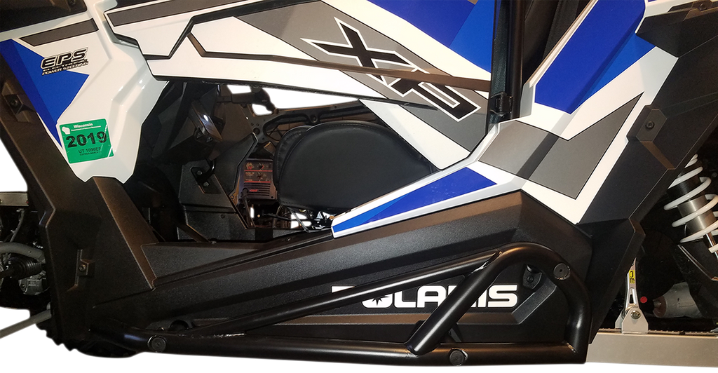 A close-up side view of a Polaris off-road vehicle features angular black, white, gray, and blue body panels, a green 2019 registration sticker, and visible suspension components. Polaris is partially visible on the lower panel.