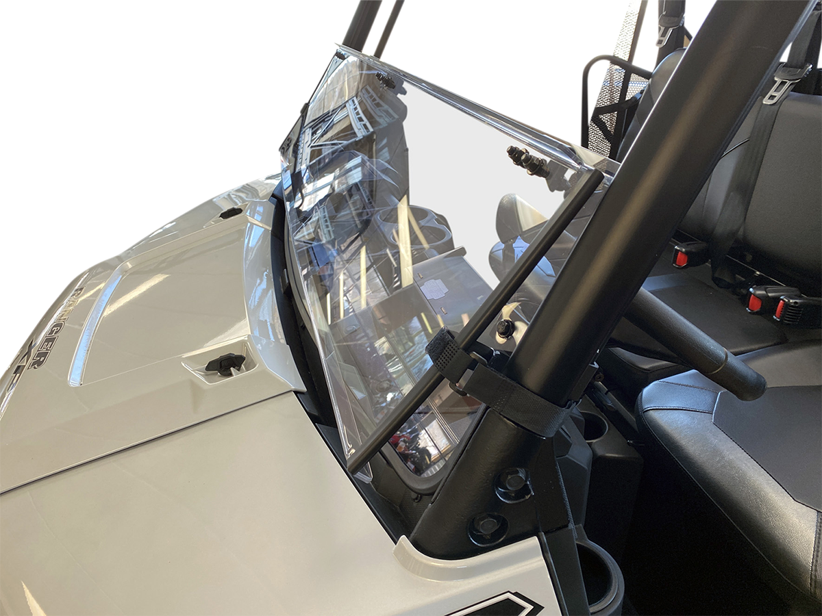 A close-up view of a clear, slightly angled windshield mounted on a white off-road utility vehicle. The windshield is attached to sturdy black bars, and the interior shows two black seats with seat belts. The background is plain and white.