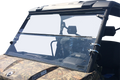 A clear, two-piece polycarbonate windshield is mounted on a camouflage-patterned utility vehicle. The windshield is held in place by metal hinges and brackets, and the background is completely white, highlighting the windshield and vehicle details.