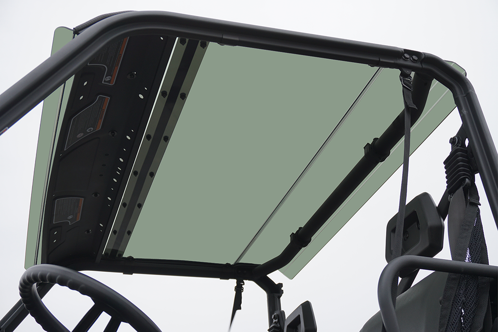 View from inside a 2016+ Can-Am Defender 500/800/1000 Single Cab, looking up at the tinted polycarbonate roof framed by a sturdy black metal roll cage, with seats and part of the steering wheel visible below against a bright sky.