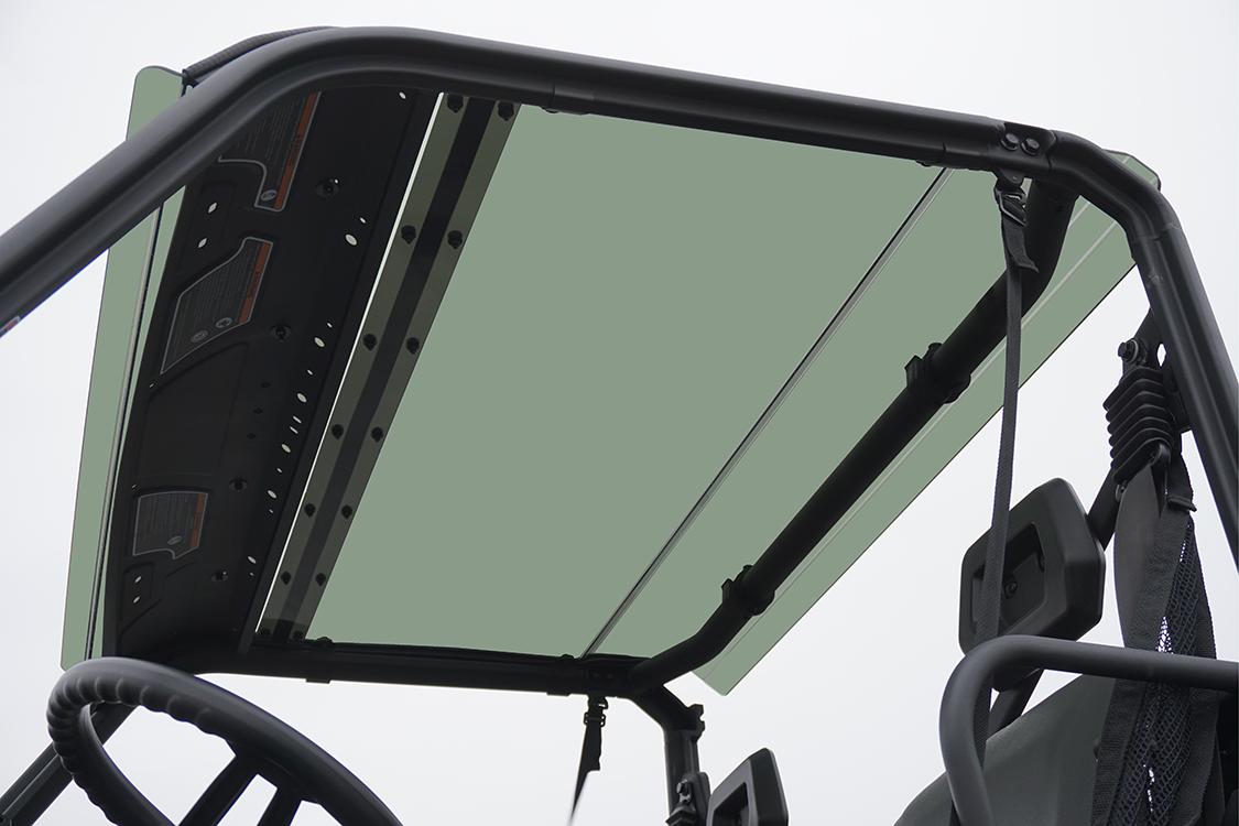 View from inside a 2016+ Can-Am Defender 500/800/1000 Single Cab, looking up at the tinted polycarbonate roof framed by a sturdy black metal roll cage, with seats and part of the steering wheel visible below against a bright sky.