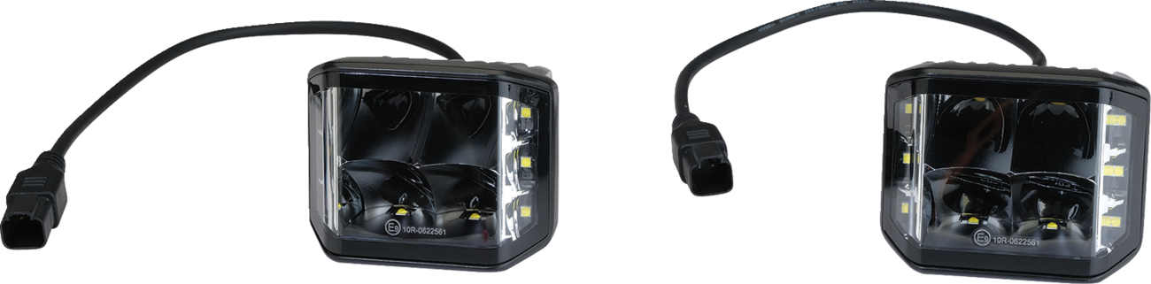 Two black square LED pod lights with clear lenses and attached black power cables, each ending in a rectangular connector. The lights feature multiple LED bulbs inside and vertical rows of smaller LEDs on both sides. The background is plain white.