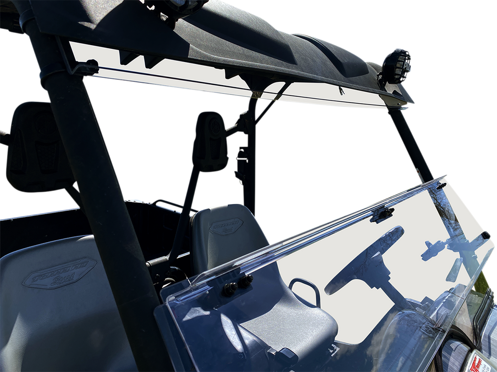 A close-up of a utility vehicle’s front interior shows two gray seats, a steering wheel, and a clear windshield with clamps. The vehicle has a black roof, overhead bars, and exterior lights mounted on top. The background is plain white.