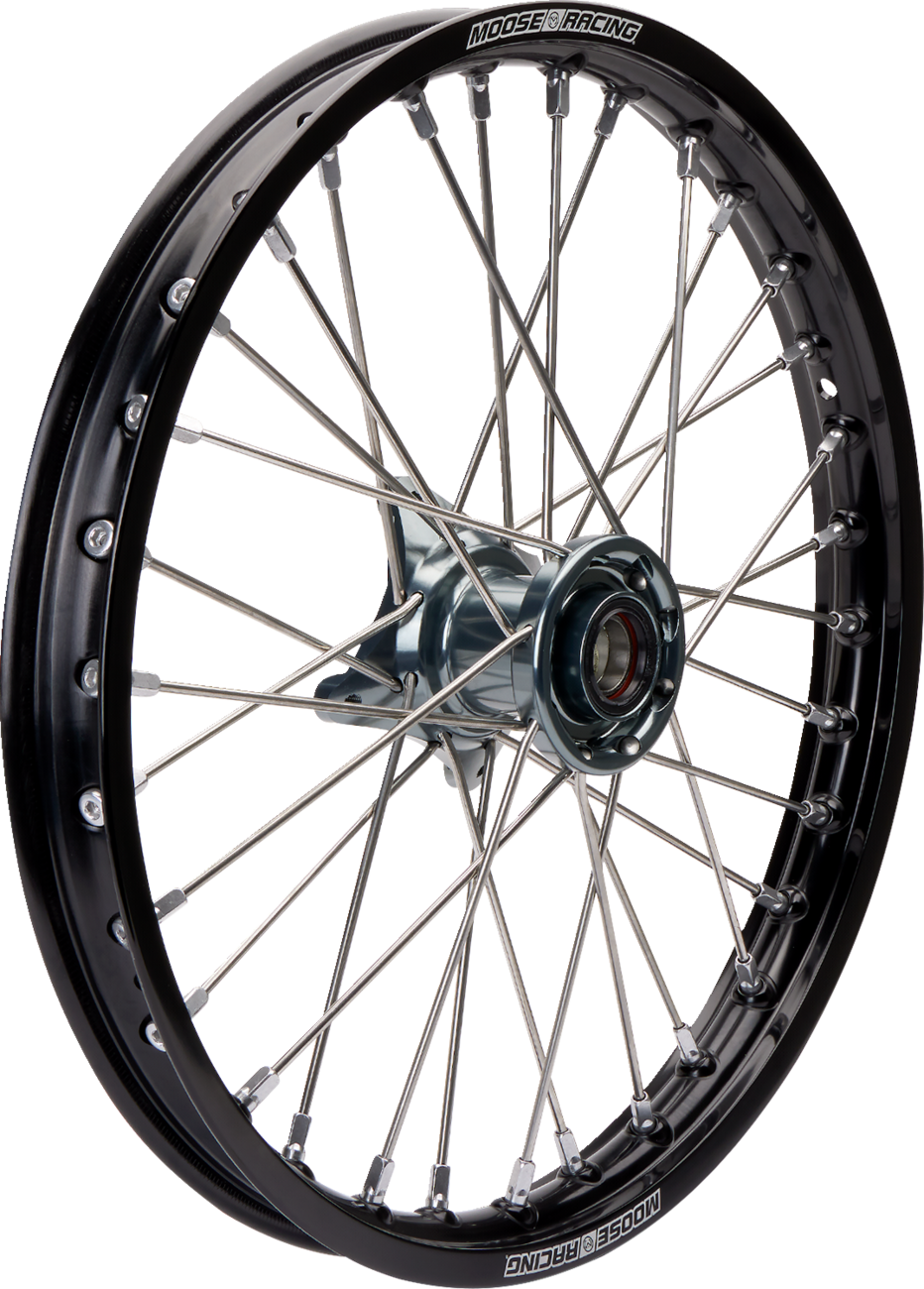 A close-up view of a black spoked motorcycle wheel rim with “Moose Racing” branding on the outer edge, metal spokes radiating from the central hub, and a shiny silver axle hole in the middle. The background is plain white.