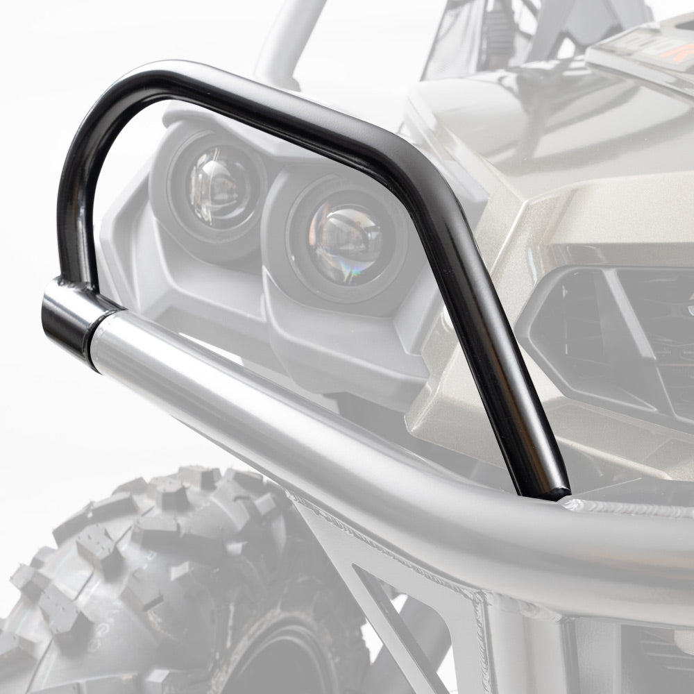 Close-up of black Can Am Commander HMF Headlight Guards (2011-2020) mounted to an ATV/UTV, with the vehicle’s headlights, grille, and rugged tire partially visible in the background. The guards are in sharp focus; the rest is faded.