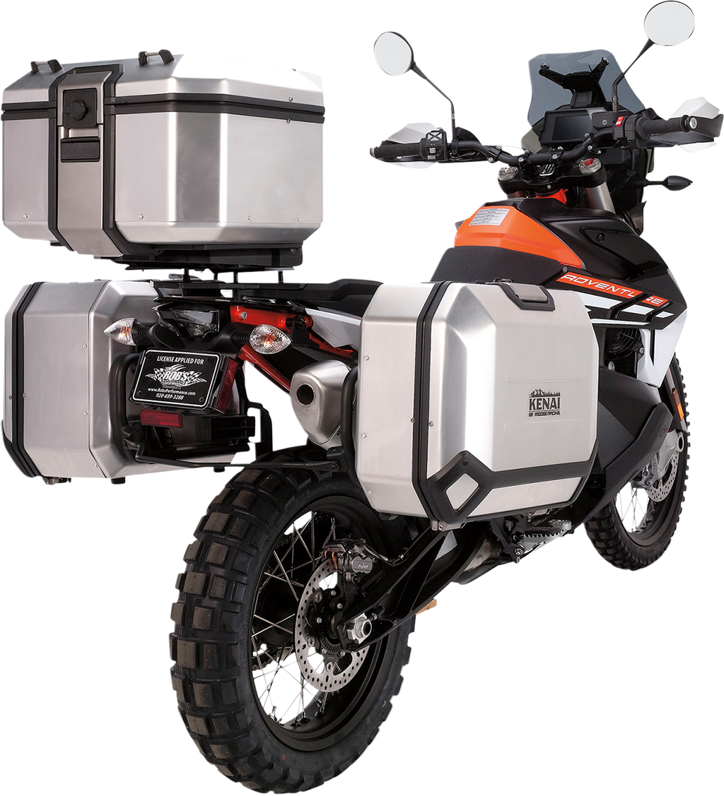 A dual-sport motorcycle with orange and black accents, equipped with three large silver hard cases for storage—one mounted on each side of the rear wheel and one on the rear rack. The bike has knobby tires and is angled from the back left.