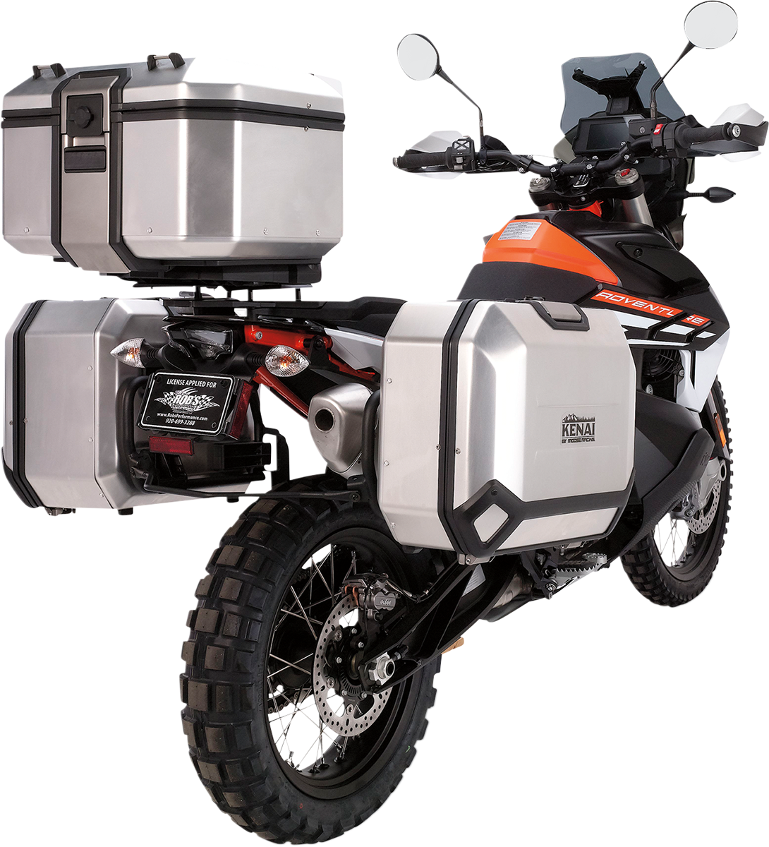 A dual-sport motorcycle with orange and black accents, equipped with three large silver hard cases for storage—one mounted on each side of the rear wheel and one on the rear rack. The bike has knobby tires and is angled from the back left.