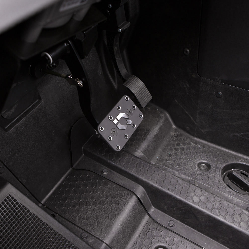 Close-up of a clean, dark driver’s footwell featuring the Polaris Rzr Rs1 HMF Brake Pedal - Black 2018+ mounted on a metal bracket, with visible screws, ridged rubber grip, and a textured black floor mat.