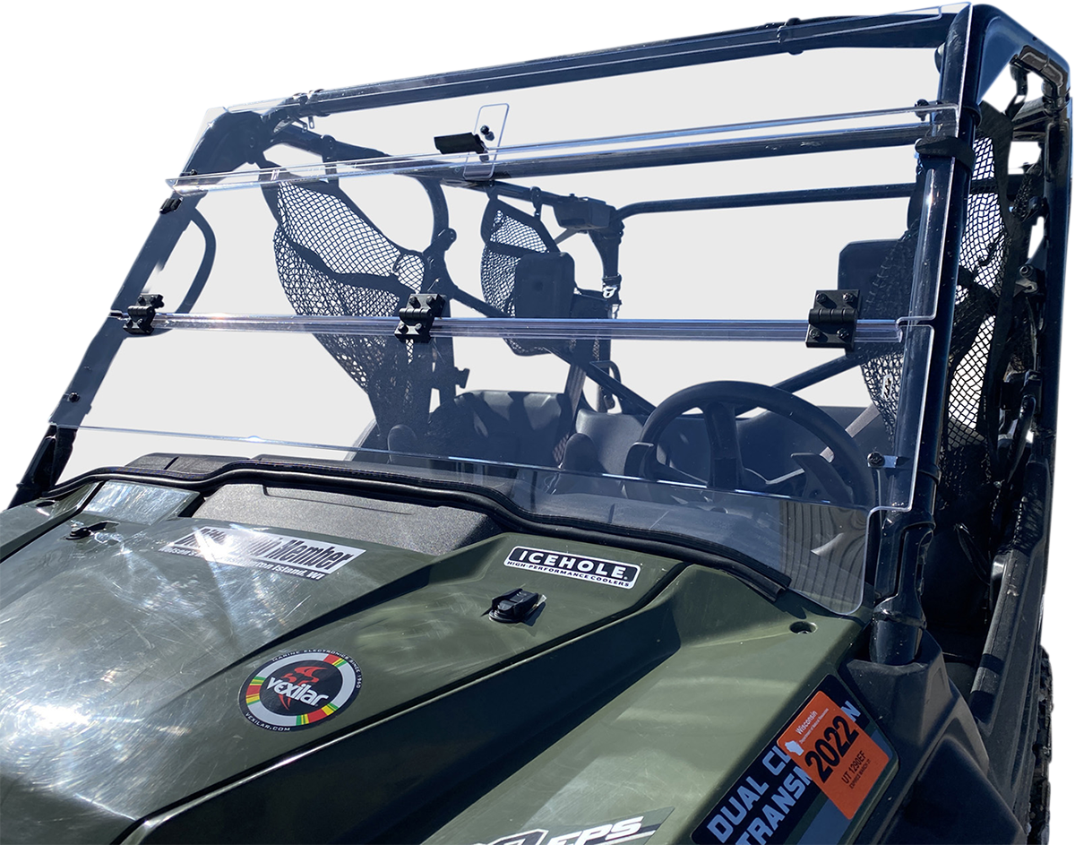 A close-up of a green off-road utility vehicle shows a clear two-piece windshield with black mounting brackets. The dashboard features various stickers, including ICEHOLE and Duel Club Frame 2022. The seats and a mesh storage pouch are visible inside.