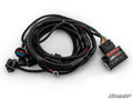 The Can-Am Maverick R Dynojet Boost Commander Kit features a coiled wiring harness with multiple connectors, a switch, and a black rectangular “SuperATV 12V ON/OFF” control module. All cables are in protective black tubing on a white background.
