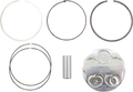 Five metallic piston rings of varying thickness and size are arranged in pairs in the top two rows, a cylindrical wrist pin is centered below them, and a reflective piston head with engraved markings is at the bottom right against a white background.