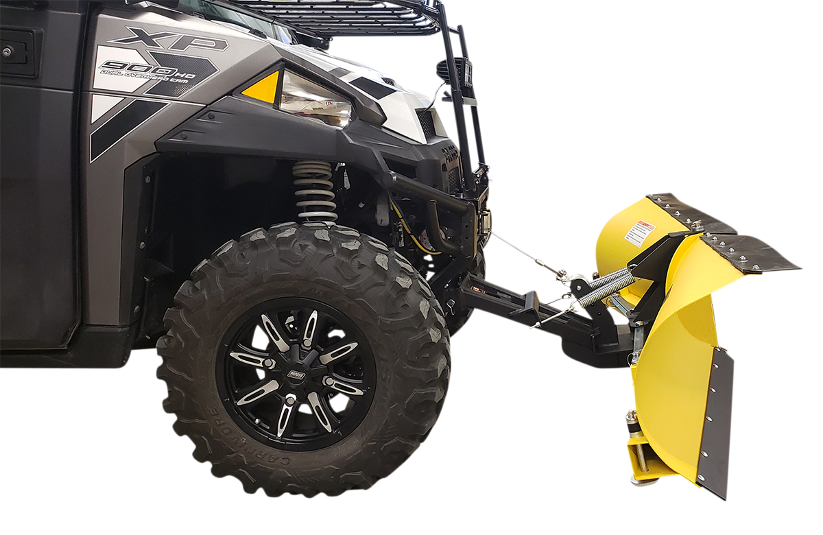 A close-up side view of an off-road utility vehicle with rugged black tires, featuring a large, curved yellow snow plow attachment mounted to its front. The plow is angled and has a black edge for scraping, with metal supports connecting it to the vehicle