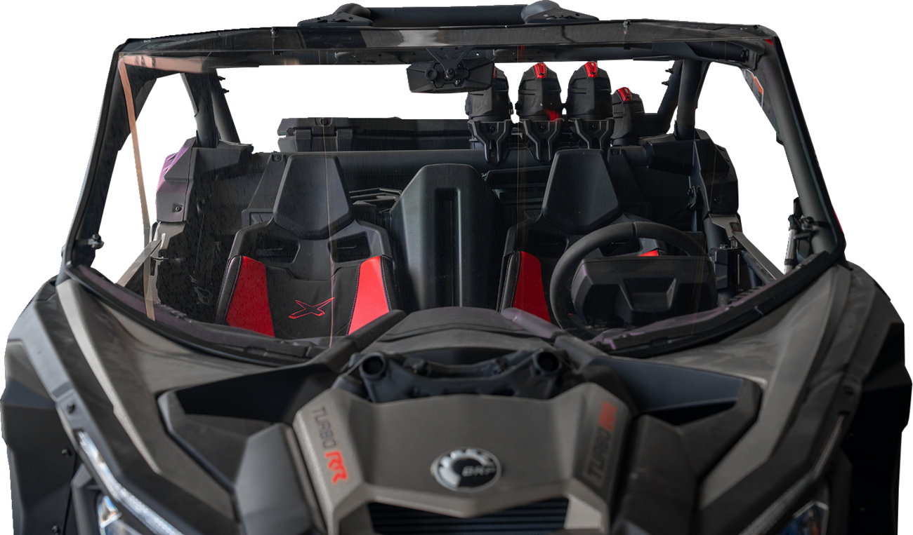 A front view of a rugged off-road vehicle with two black and red bucket seats, a steering wheel on the right, and three helmets secured behind the seats; the windshield and vehicle interior appear dusty.