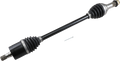 A black automotive drive shaft with metal ends and rubber CV joint boots is shown diagonally on a light background. A small metal pin lies nearby for scale. The shaft is clean and appears new, with visible grooves and mechanical details.
