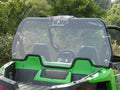 A close-up of the front seats and steering wheel, viewed from the cargo bed of an off-road vehicle equipped with an Arctic Cat / Textron Wildcat Trail Lexan Rear Panel. The vehicle is outdoors, surrounded by green trees and bushes.