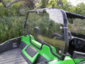 An Arctic Cat Wildcat Trail And Sport with a Lexan Back Panel is parked outdoors among trees and vegetation. Its interior, featuring black seats and dashboard, is visible through the windshield.