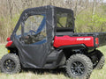 A red Can-Am side-by-side with rugged tires is parked on grass, featuring the Offroad Armor Can-Am Defender Soft Full Doors Kit with black soft doors and clear windows, set against sparse trees and green shrubbery.
